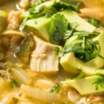 A bowl of spicy Chili Chicken Soup garnished with fresh herbs, served with a slice of lime on the side.