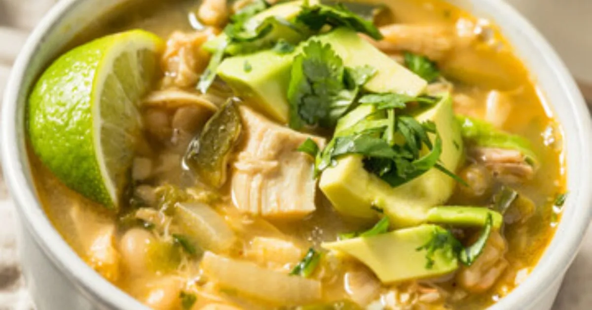 A bowl of spicy Chili Chicken Soup garnished with fresh herbs, served with a slice of lime on the side.